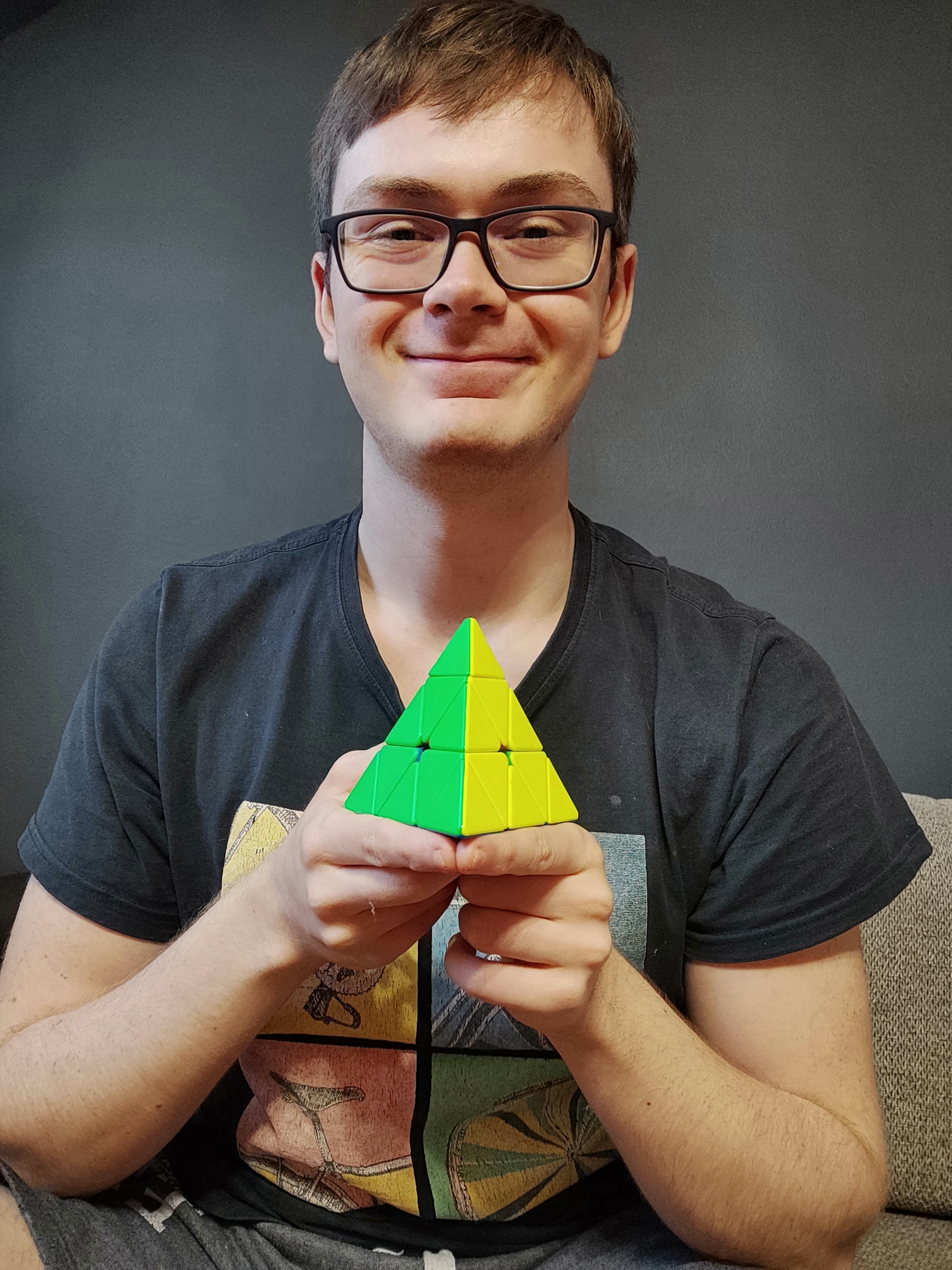 Mężczyzna trzyma w ręcę ułożoną łamigłówkę Pyraminx.